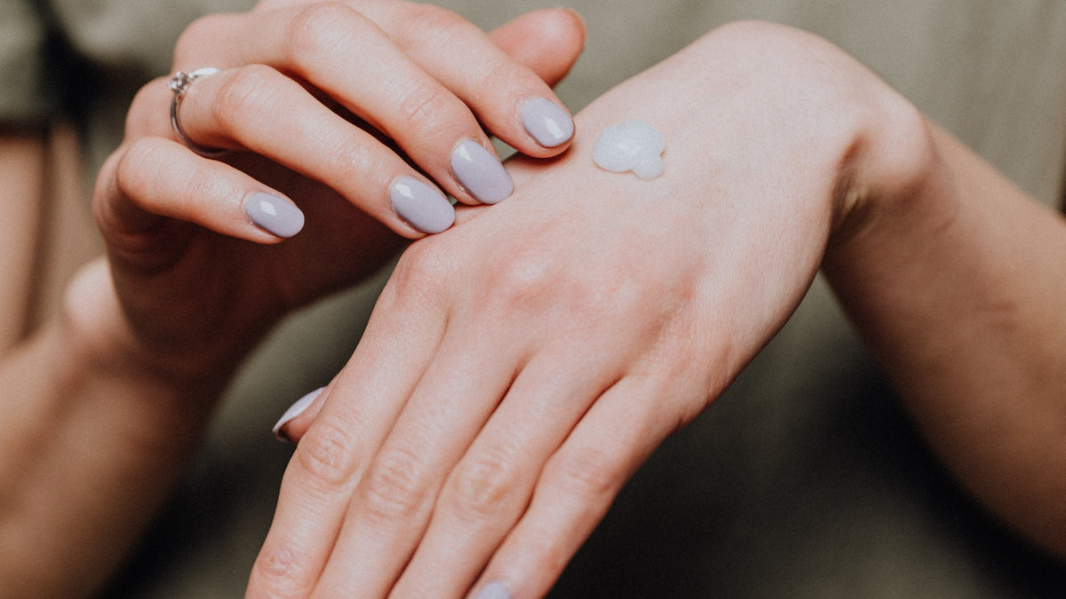Hands smoothing moisturizer over the back of a hand, olive knit