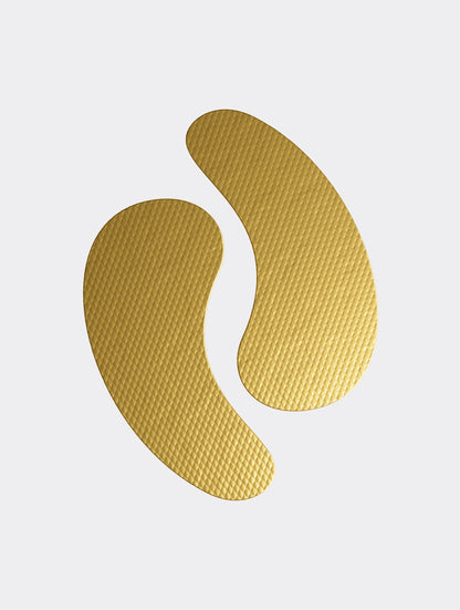 A pair of gold AGELESS hydrogel eye patches, crescent-shaped with a fine textured surface, on a pale grey ground.