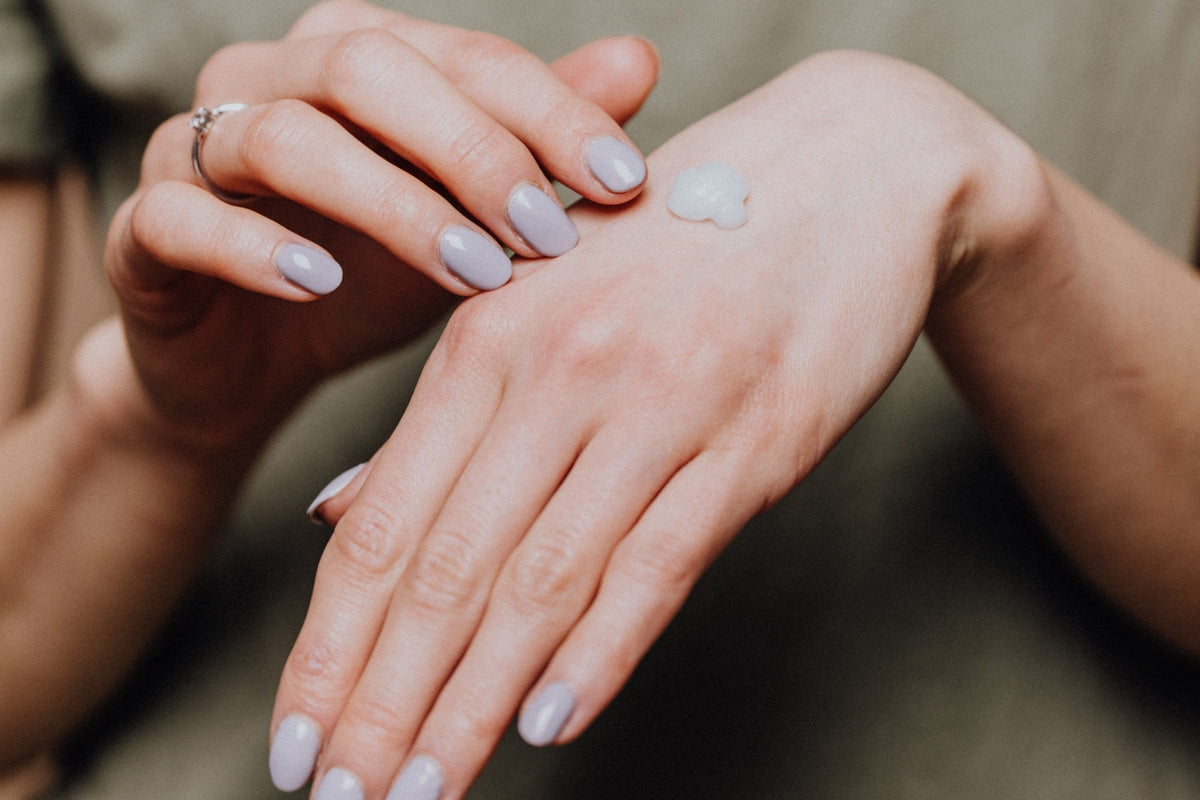 Hands smoothing moisturizer over the back of a hand, olive knit