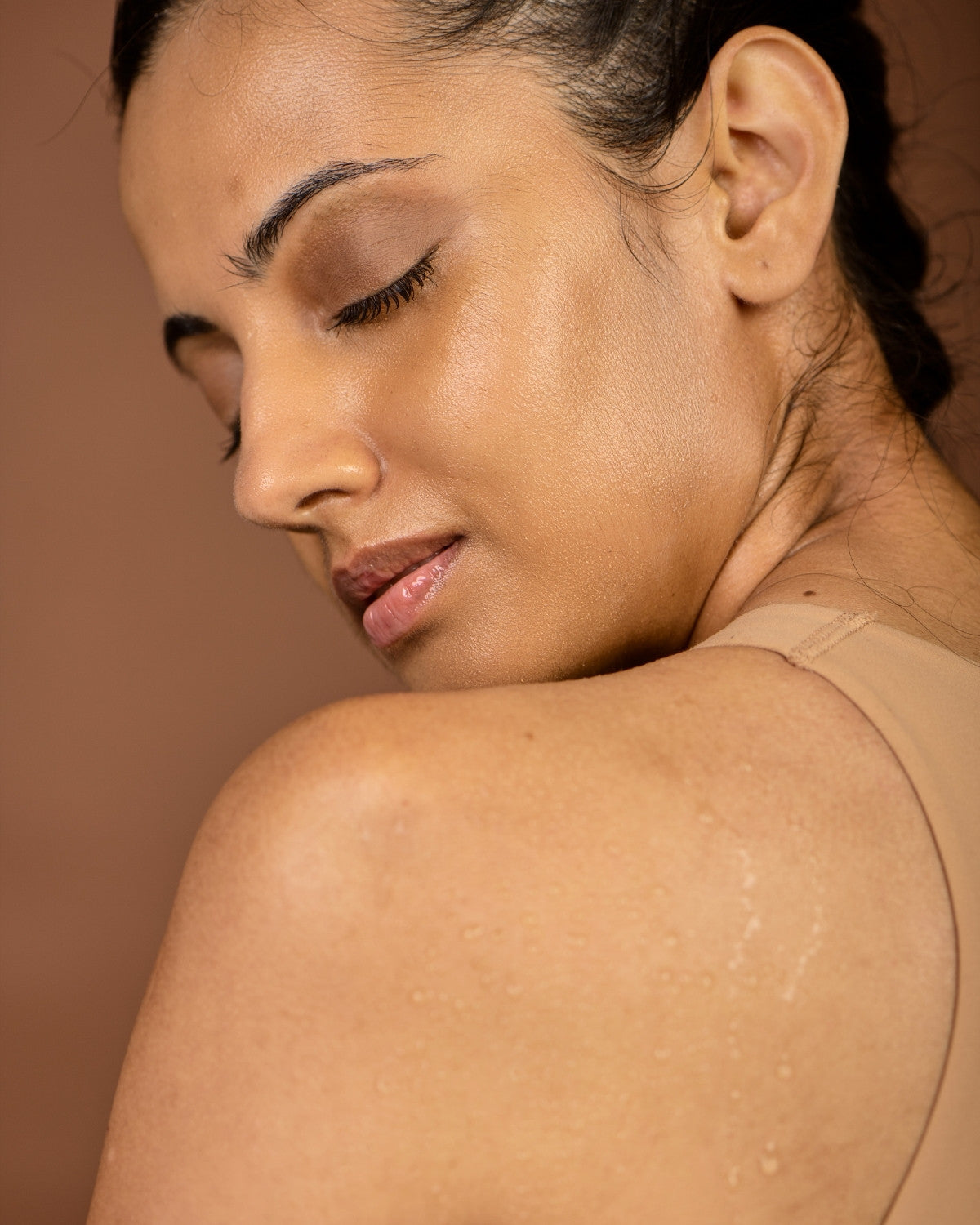 Woman with eyes closed looking over her bare shoulder, warm neutral wall