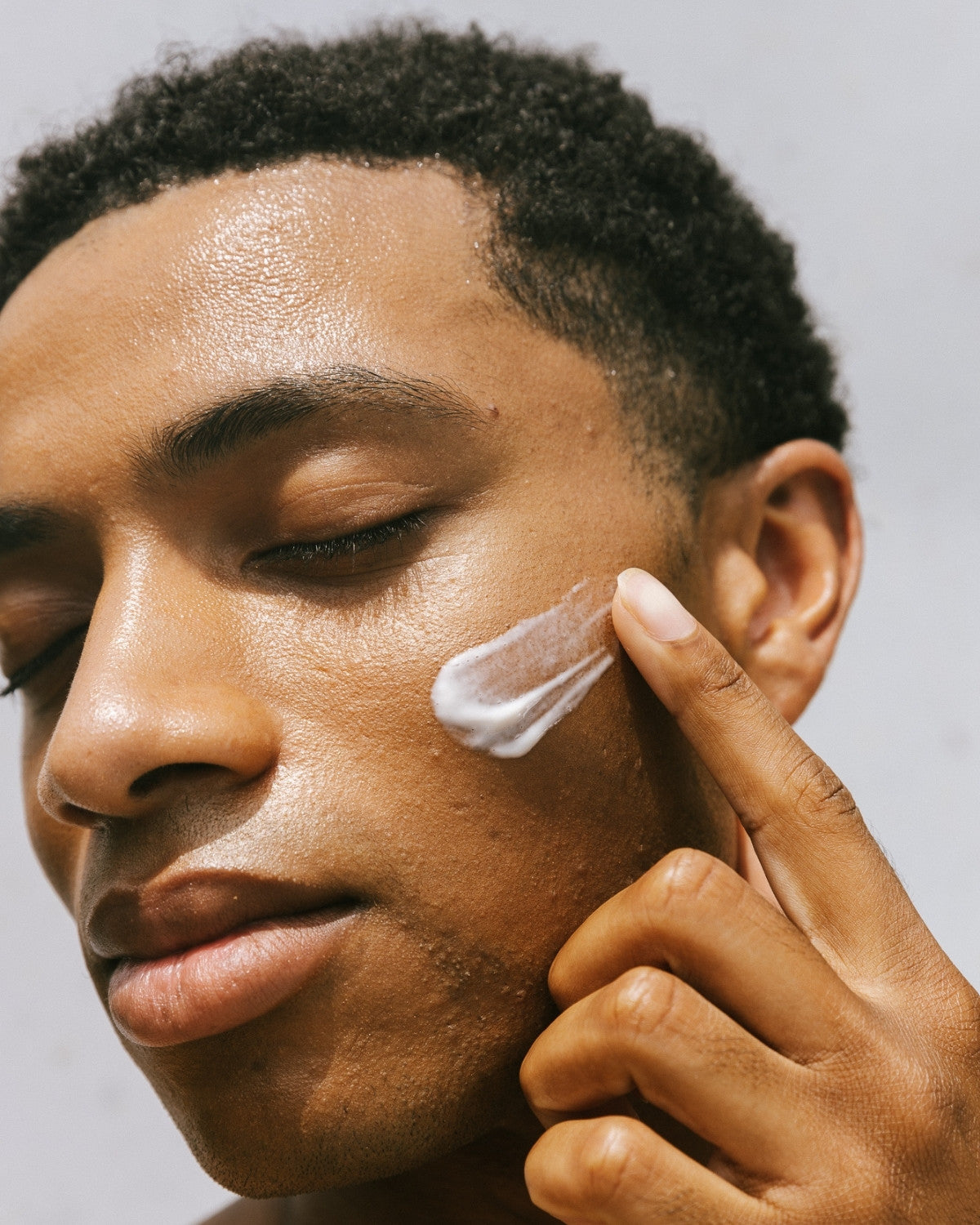 Man pressing moisturizer into his cheek, eyes closed, natural light