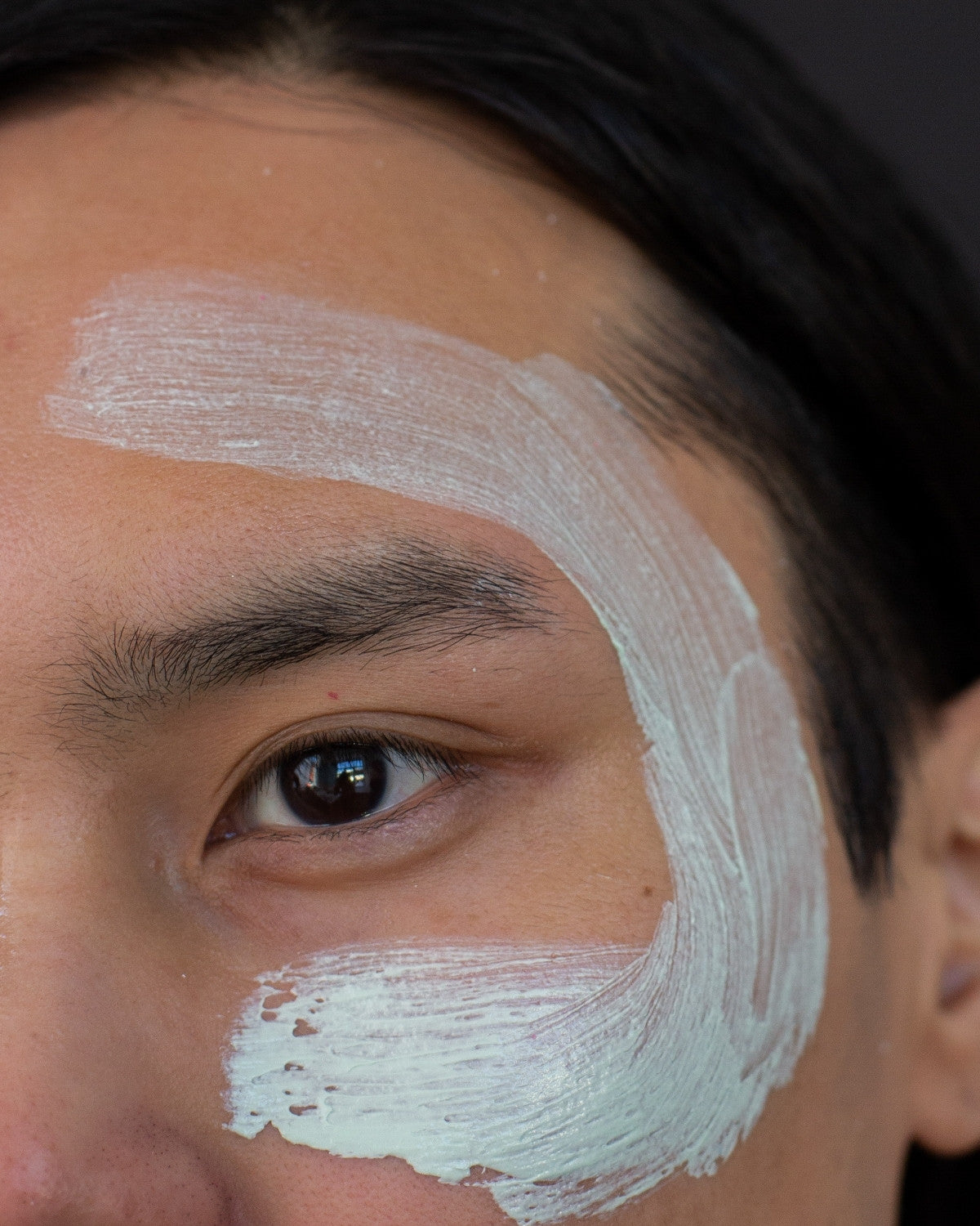 Close crop of a man with a swipe of clay mask across his cheek