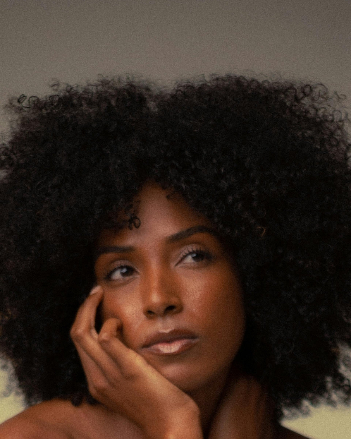 Woman with curly hair resting her cheek on her hand, soft studio light