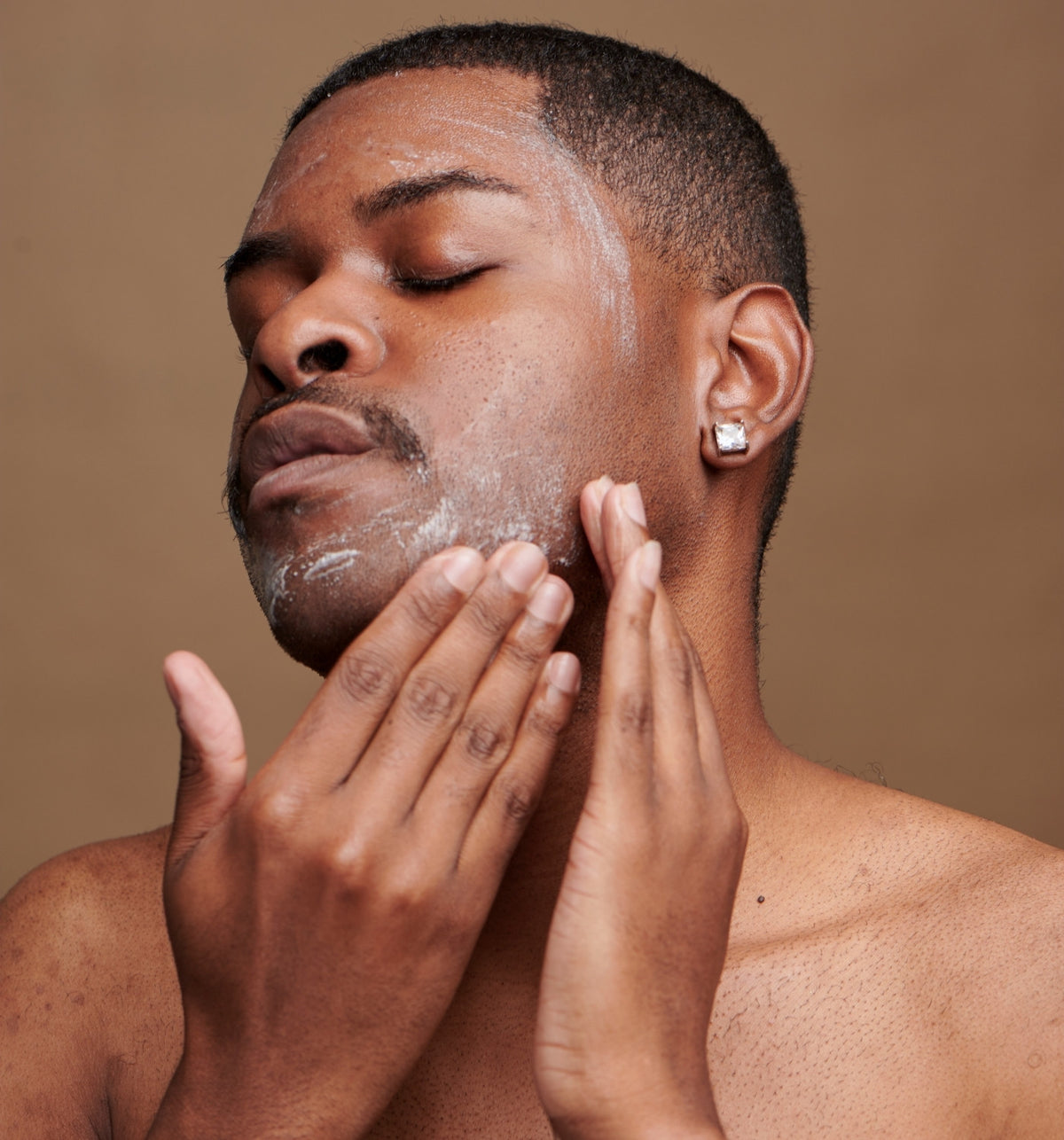 Man cleansing his jaw with both hands, eyes closed, warm taupe backdrop