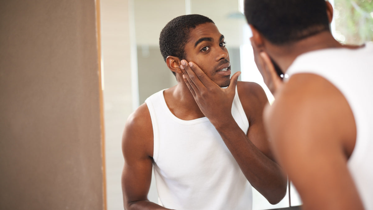 Man checking his skin in the bathroom mirror, hand on his cheek, natural light
