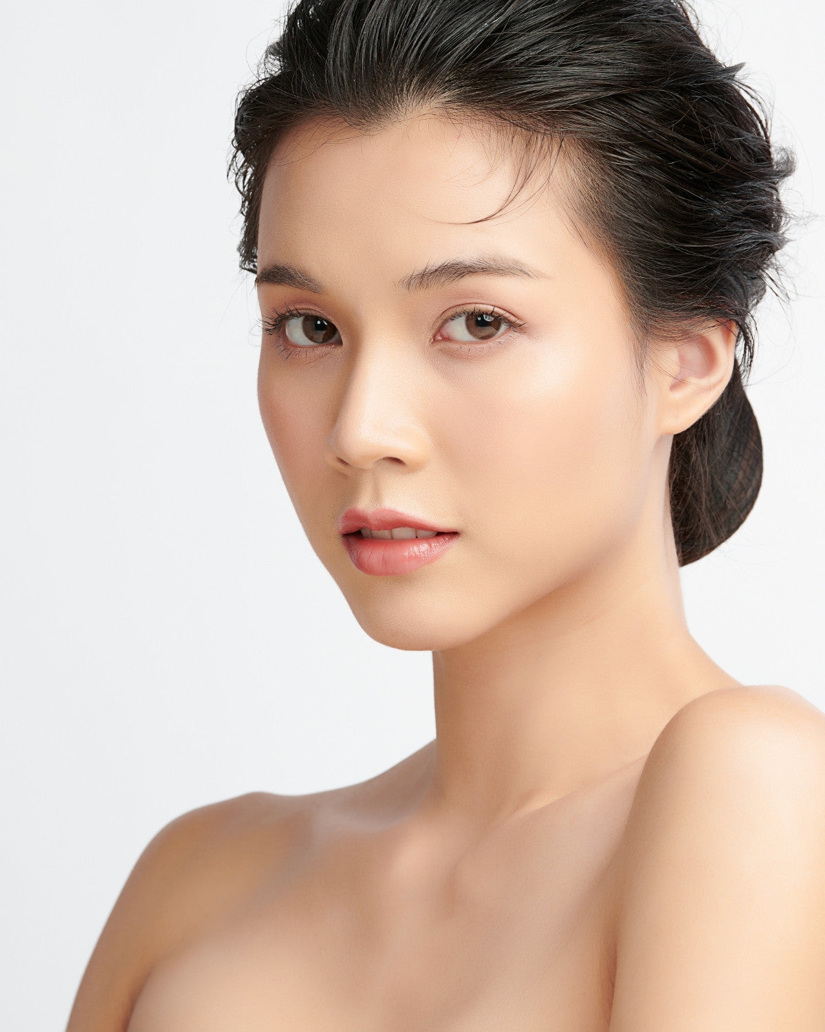 Woman with hair pulled back, bare shoulders, direct gaze, white studio backdrop