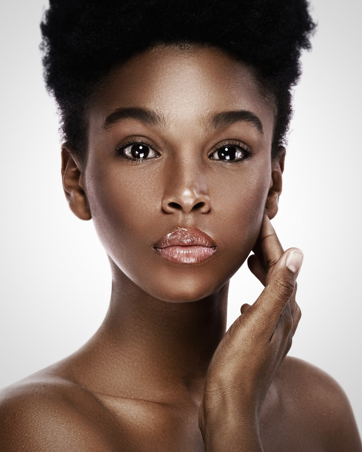 Young woman with short natural hair, direct gaze, hand at chin, soft grey studio backdrop