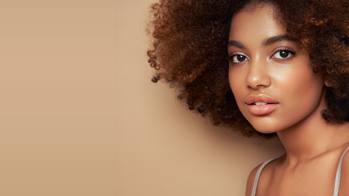 Young woman with natural curly hair, direct gaze, warm beige backdrop